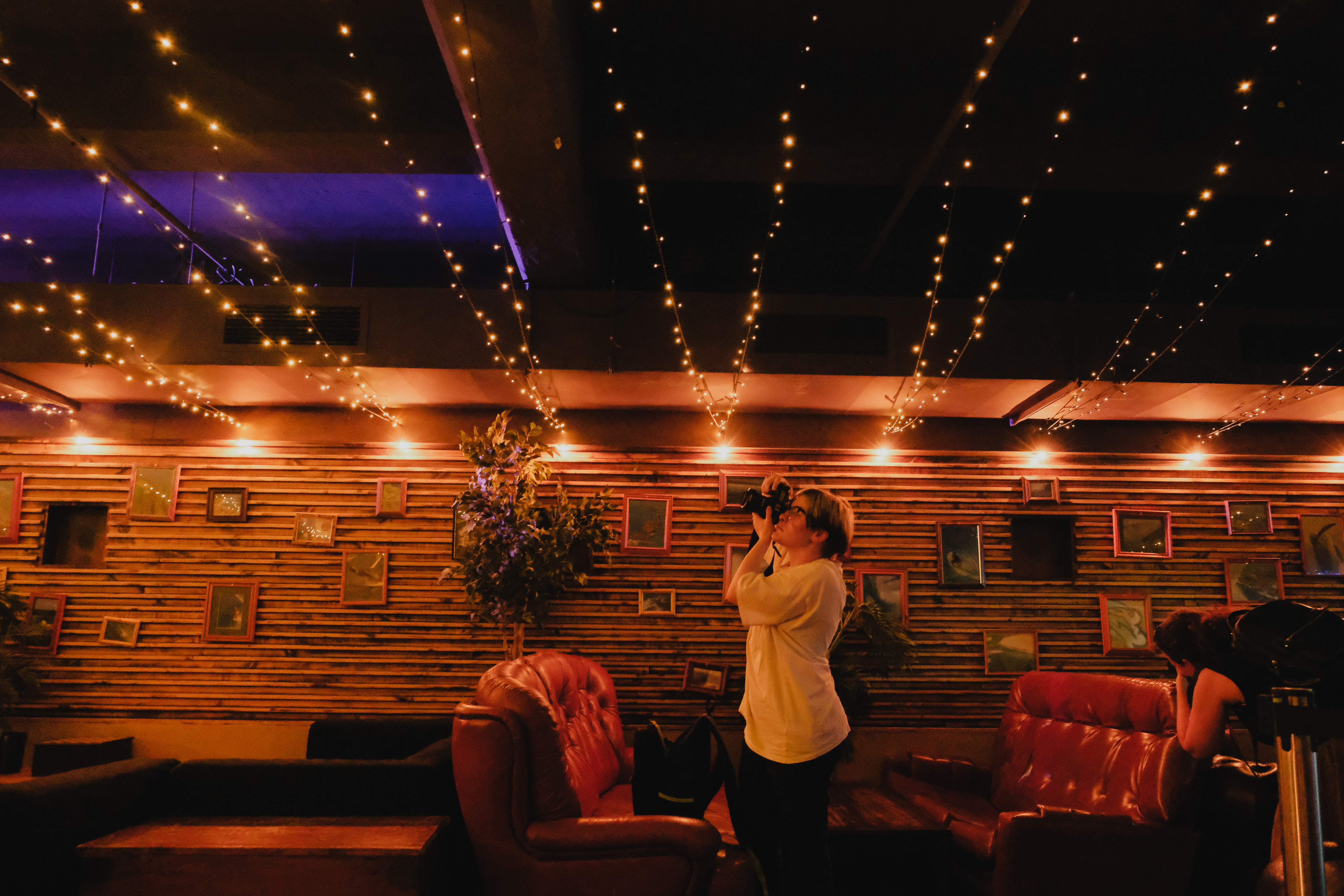 Collarts photography student pointing camera to night sky with fairy lights hanging above