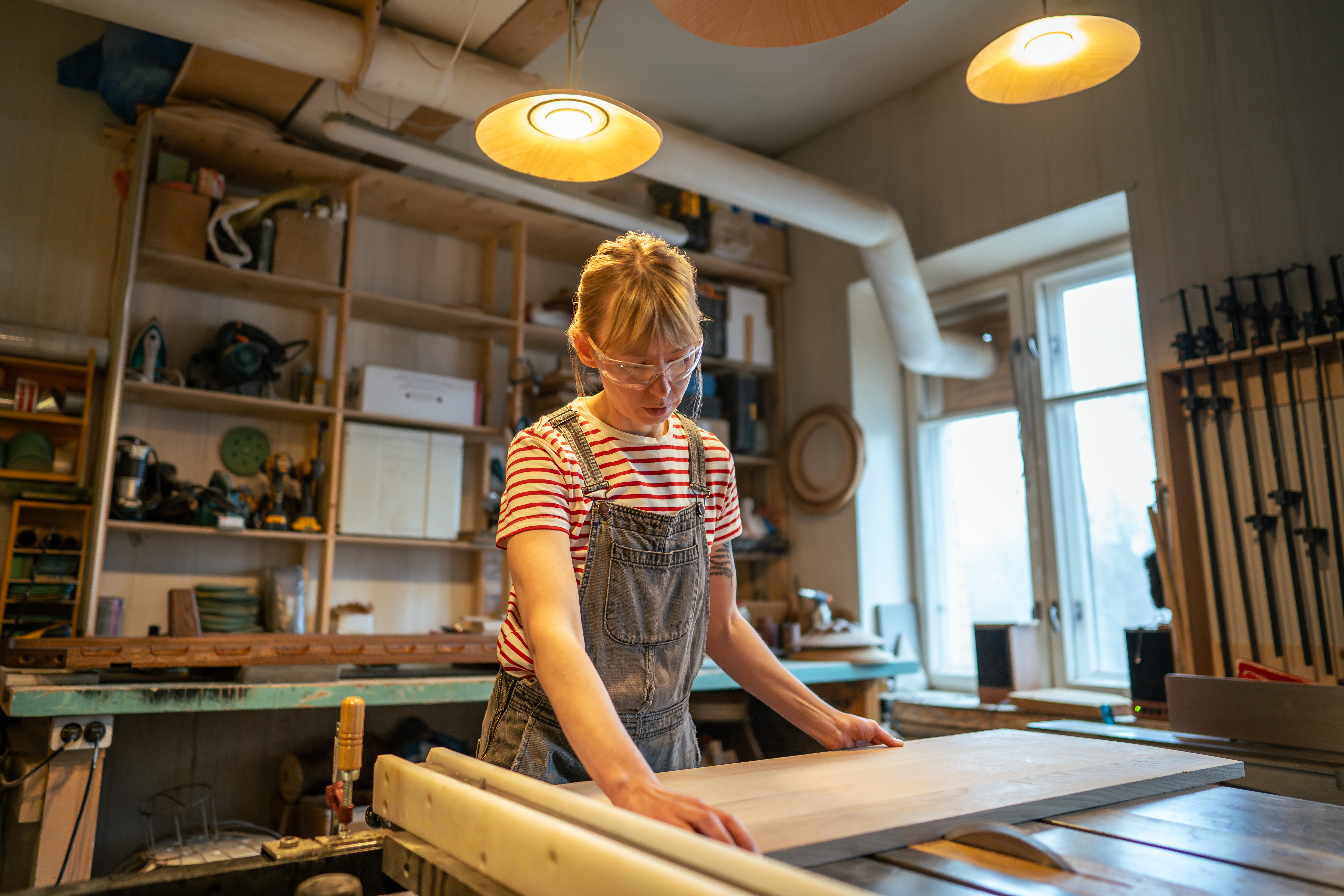Woman furniture maker in workshop measuring a piece of wood