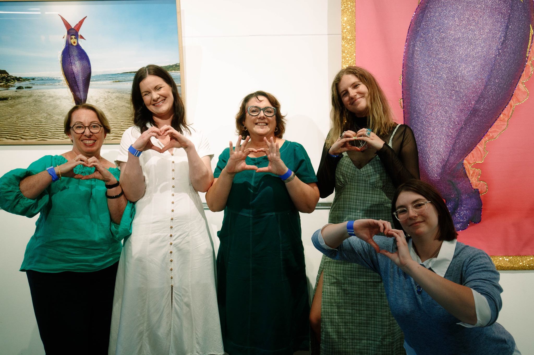 Group of Collarts students and teachers smiling and posing with wall of art behind them