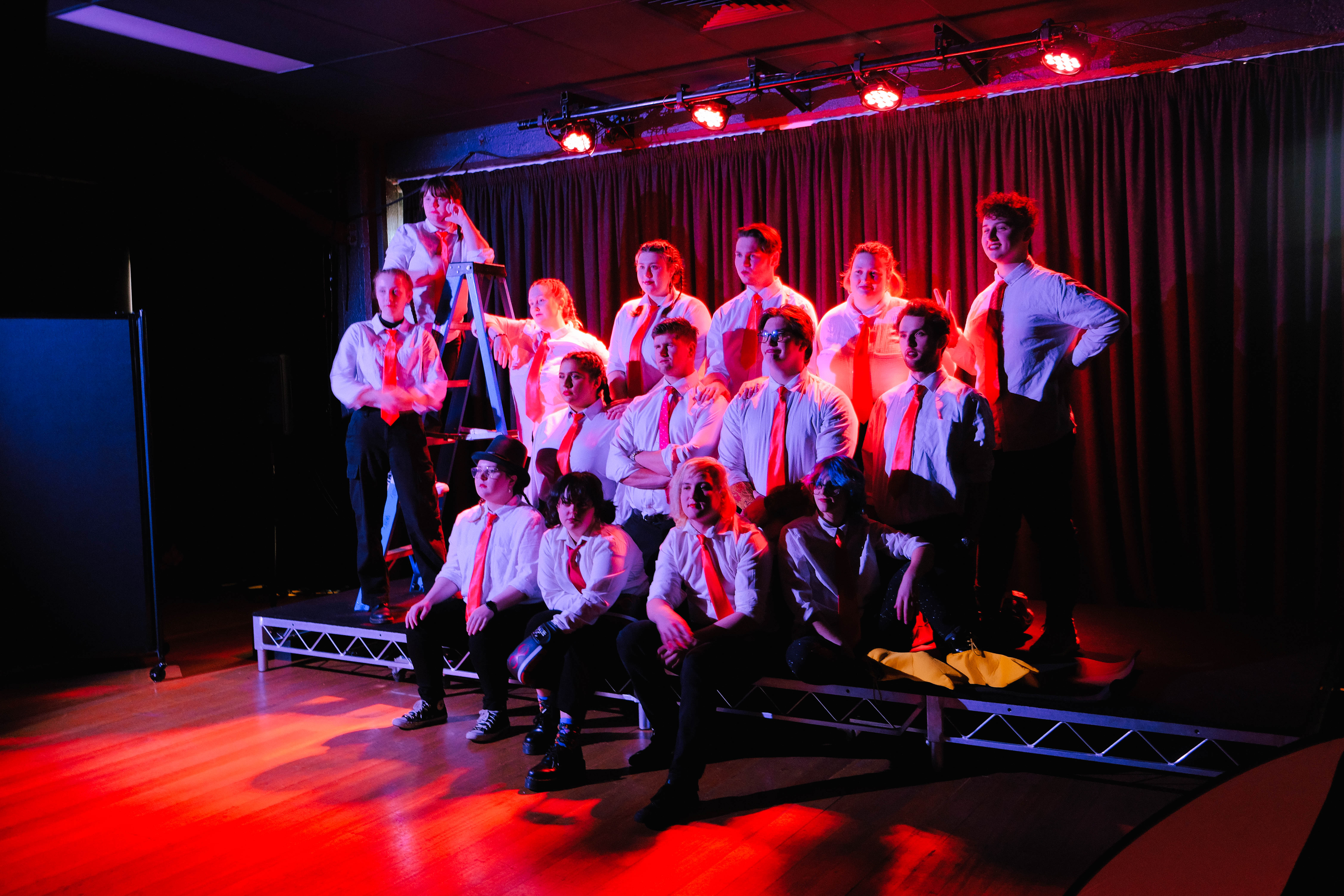 Group of Collarts acting students standing and posing on stage all wearing white shirts, red ties and black pants