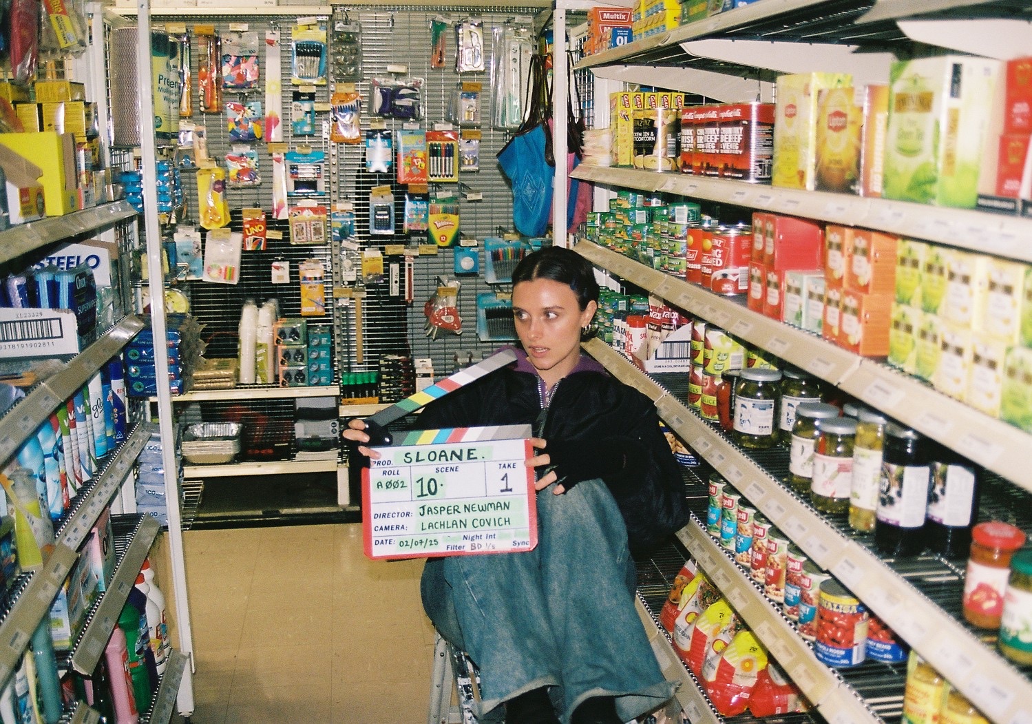 Collarts acting student sitting on a stool in a supermarket aisle holding a clapper board