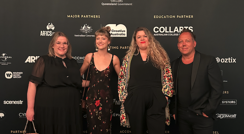 Four Collarts teachers standing and smiling in front of a media wall at industry event
