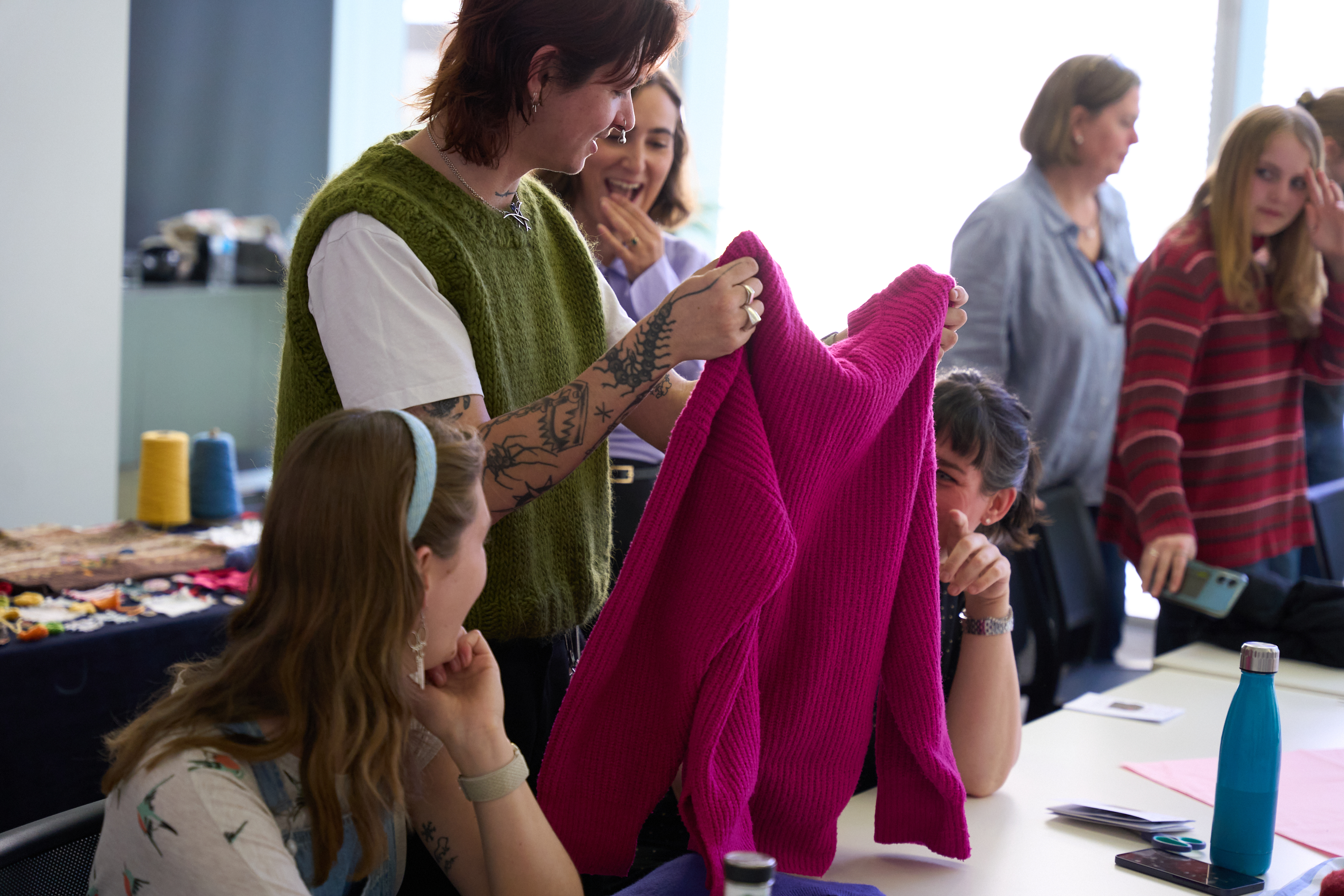 Two Collarts fashion students holding up a pink sweater they helped repair as part of the Melbourne Fashion Week & Thread Together partnership. 