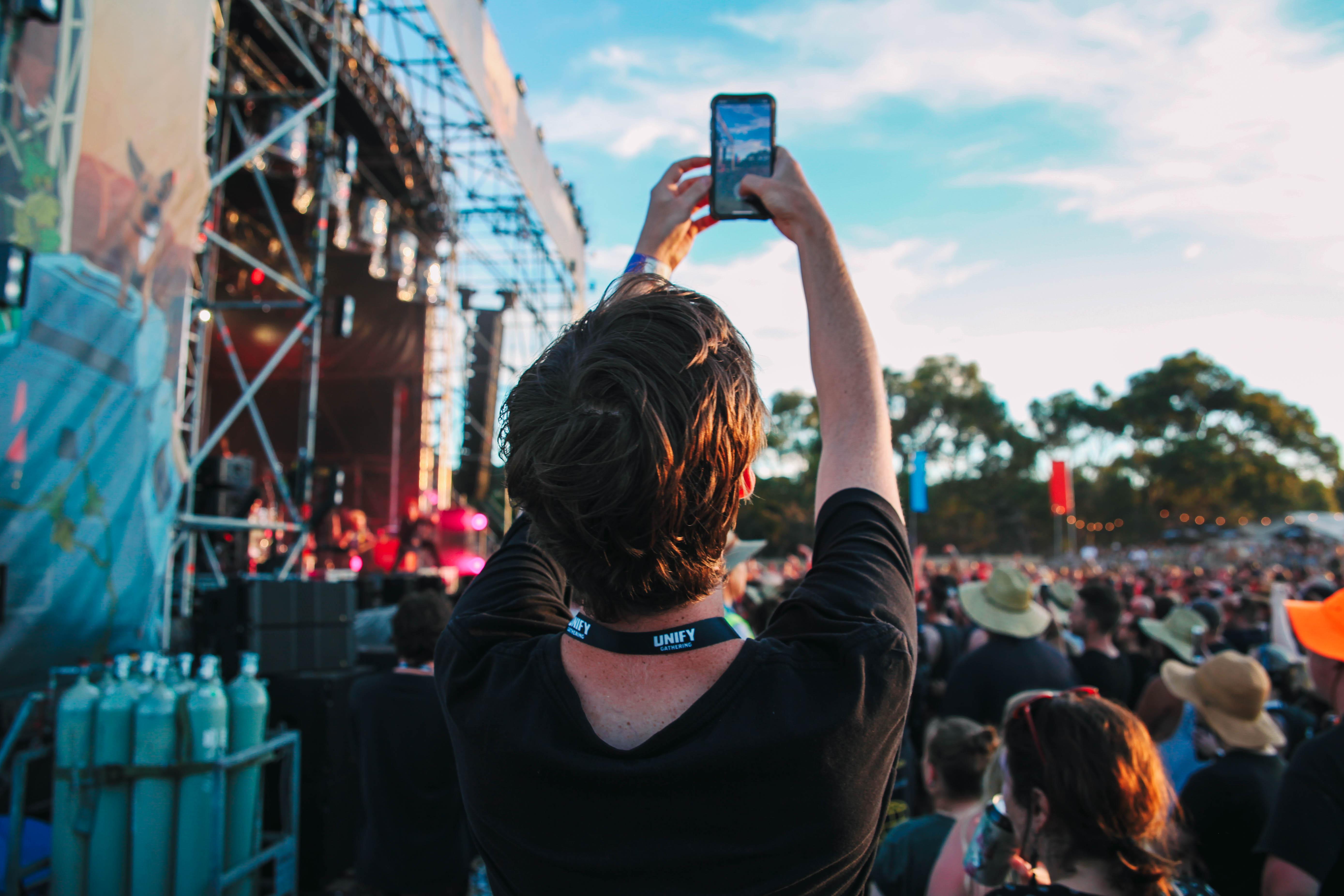 A person taking a photo on their phone of a crowd at a music festival